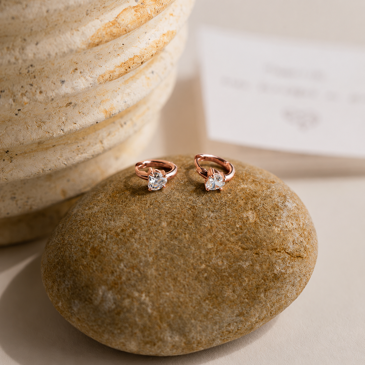 Rose gold earrings with clear gemstones on a stone surface