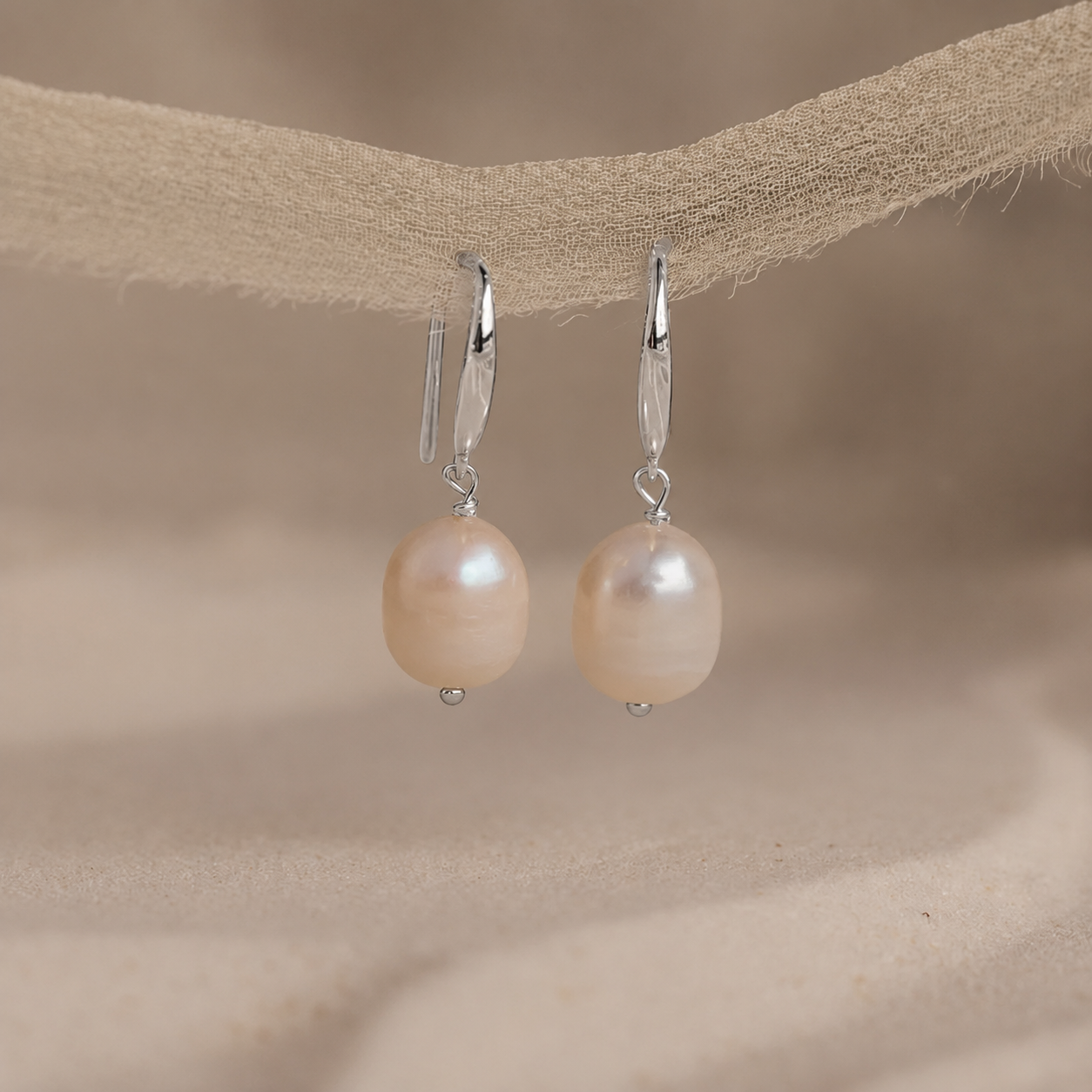Pearl earrings hanging on a beige fabric background