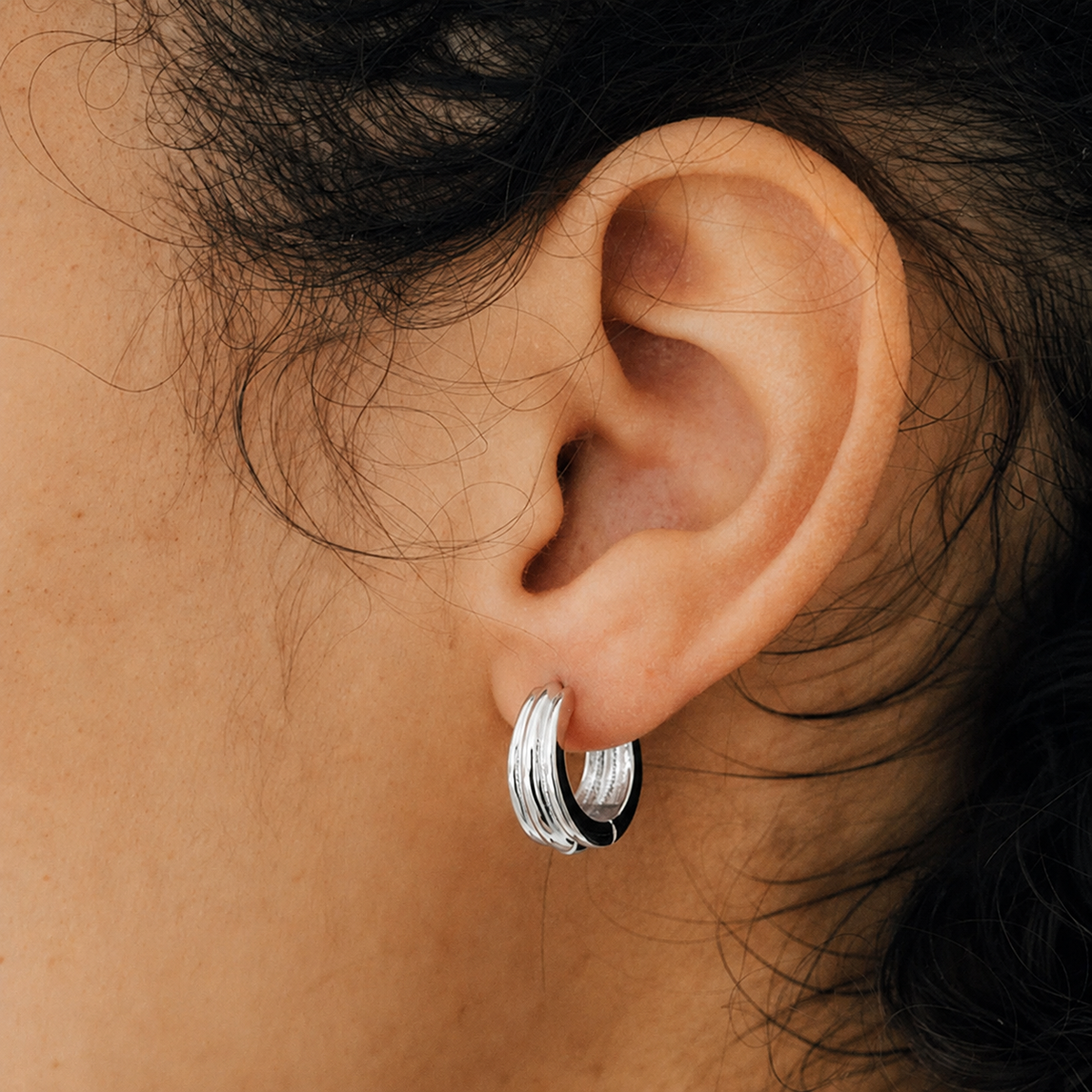 Close-up of an ear wearing a silver hoop earring with hair partially covering the frame.