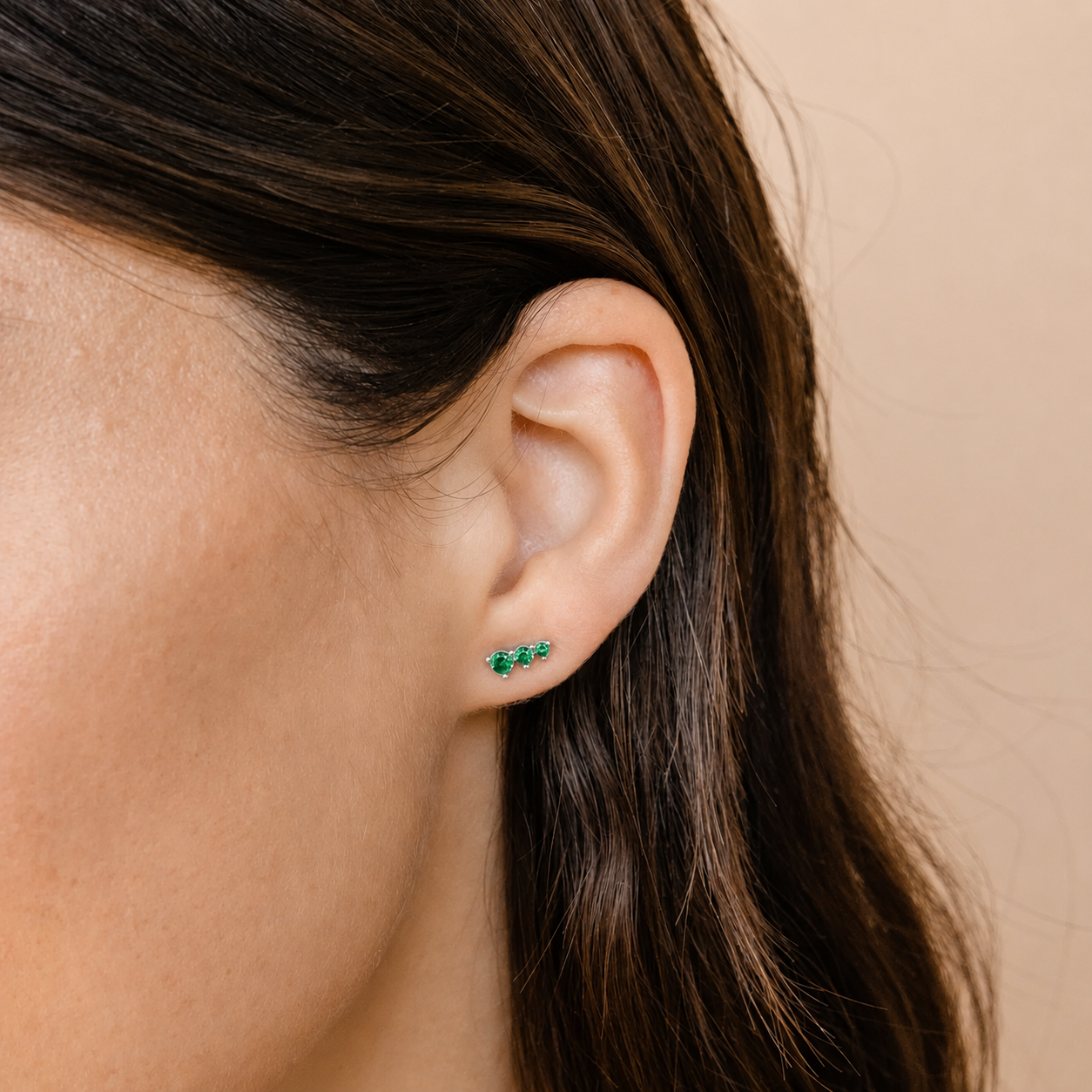 Close-up of an ear wearing green earrings with a neutral background