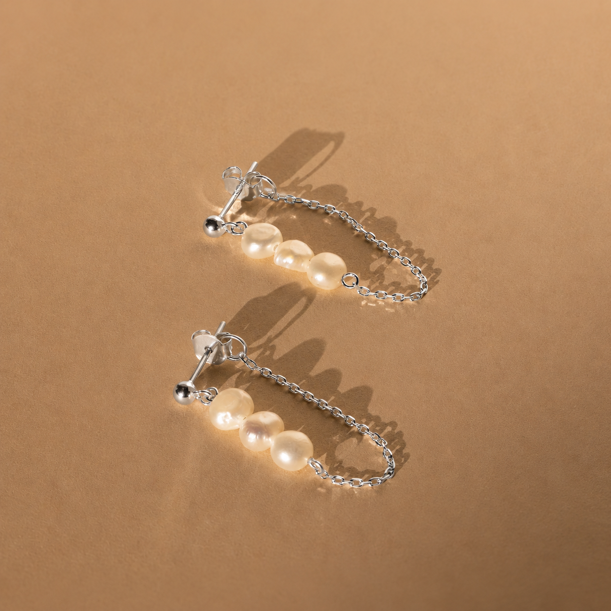 Pair of pearl earrings with silver chains on a brown background