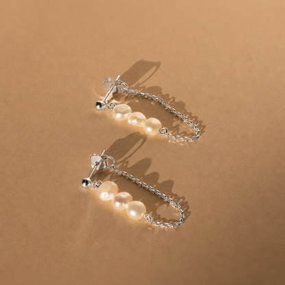 Pair of pearl earrings with silver chains on a brown background