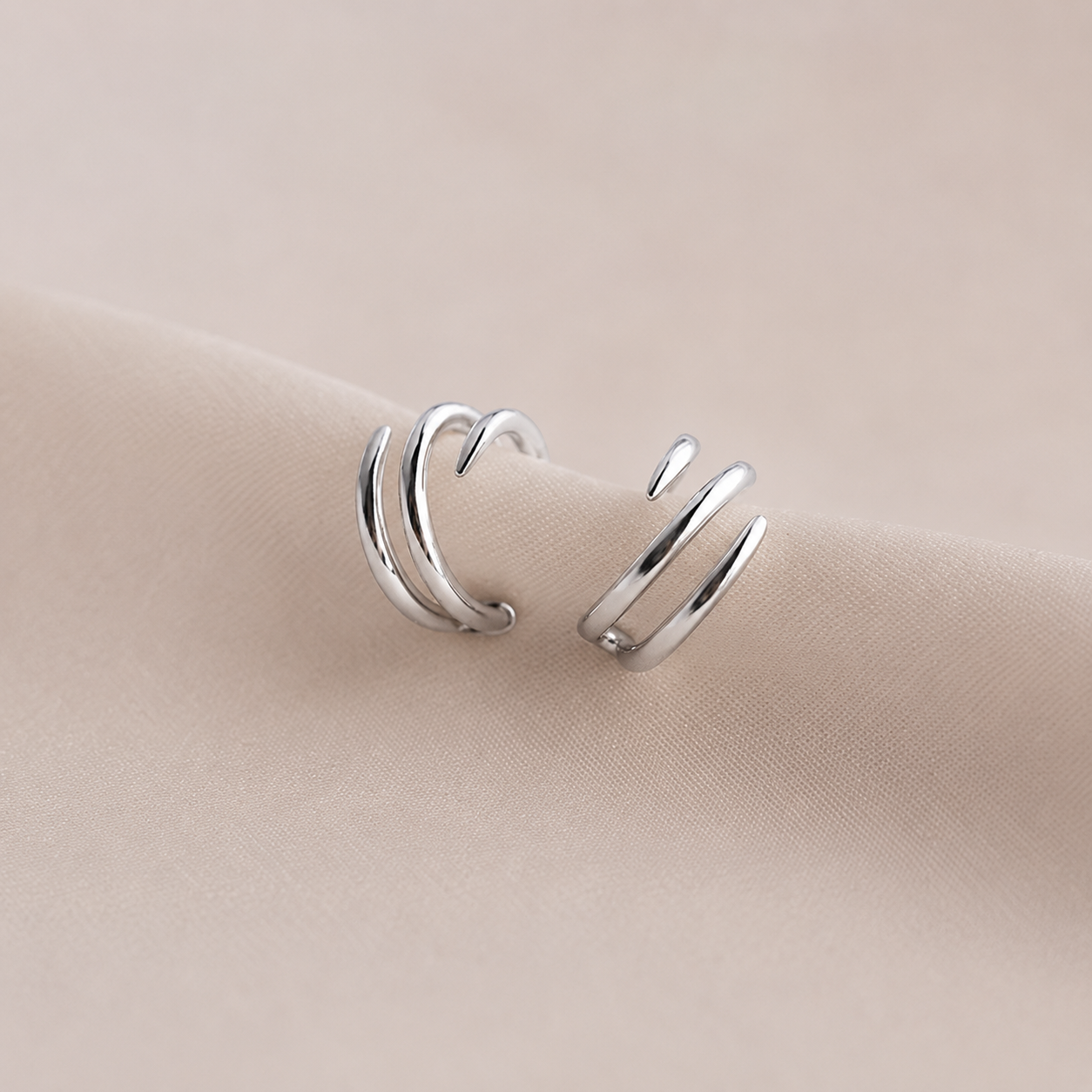 Pair of silver ear cuffs on a beige fabric background