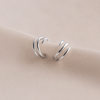 Pair of silver ear cuffs on a beige fabric background