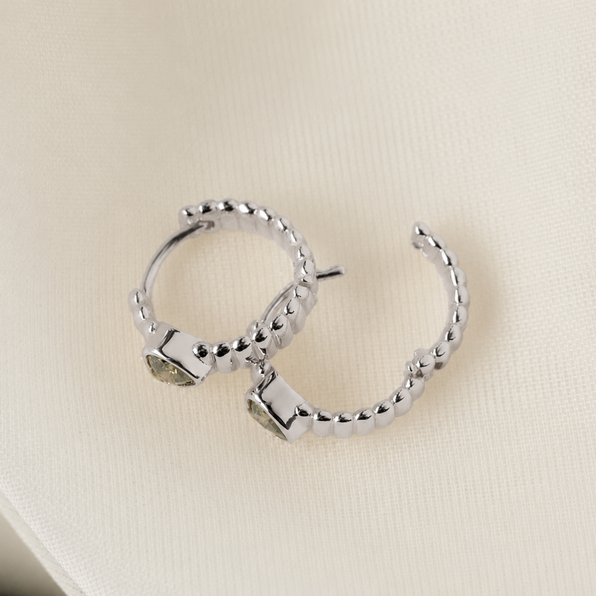 Silver hoop earrings on a beige fabric background