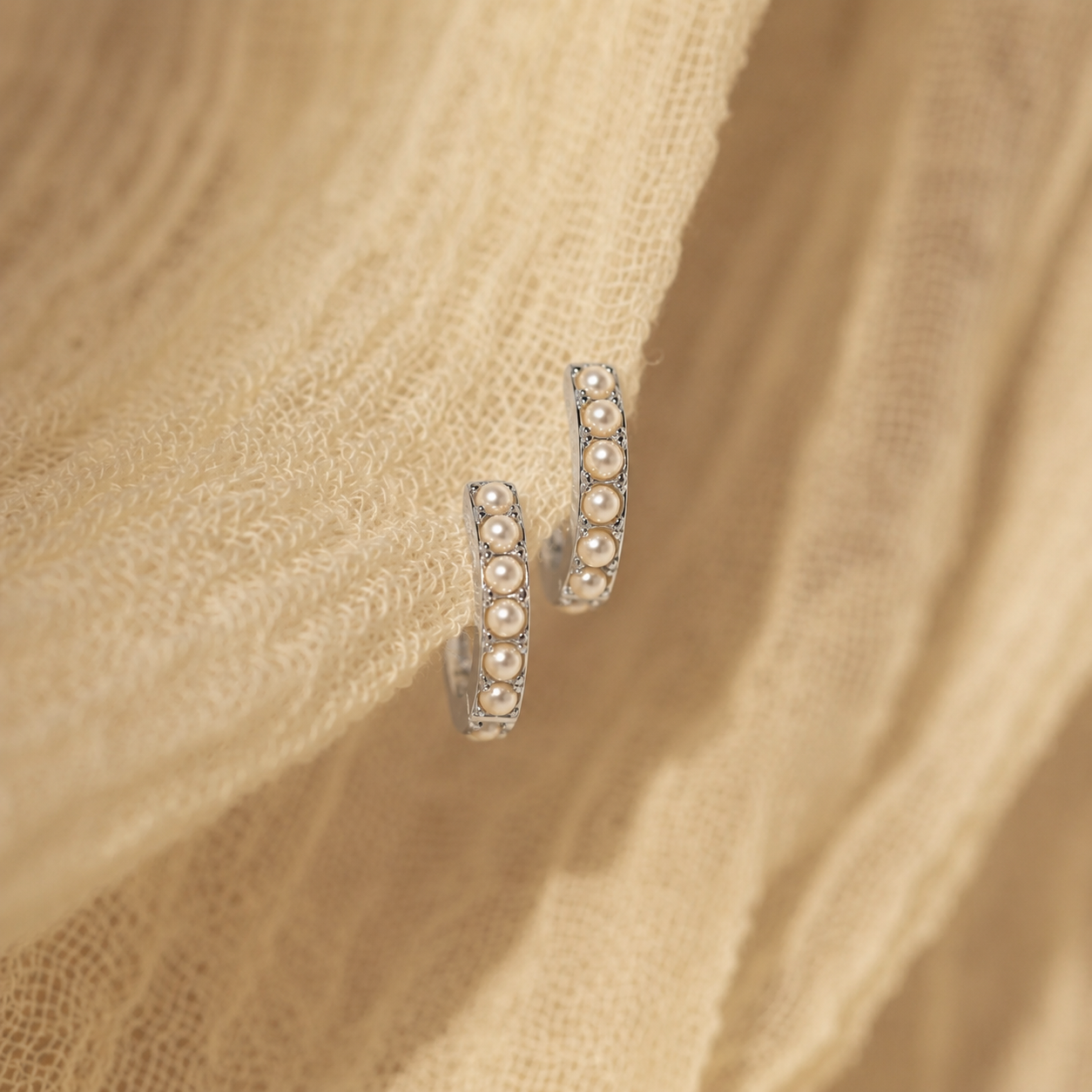Pair of pearl hoop earrings on a beige fabric background