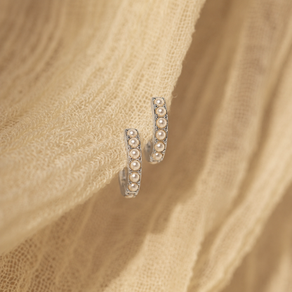 Pair of pearl hoop earrings on a beige fabric background