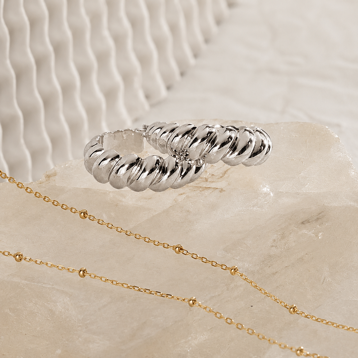 Silver ring and gold chain on a textured beige surface