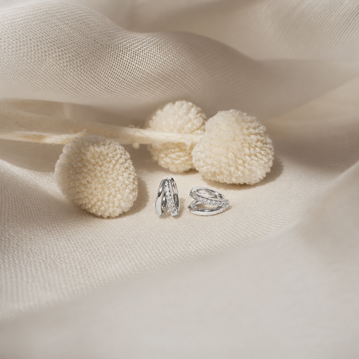 Two silver-toned textured rings displayed on a soft cream fabric backdrop with decorative dried pom-pom flowers.
