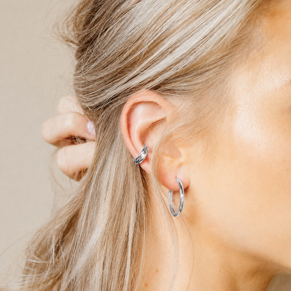 Close-up of a person wearing silver hoop earrings with a neutral background