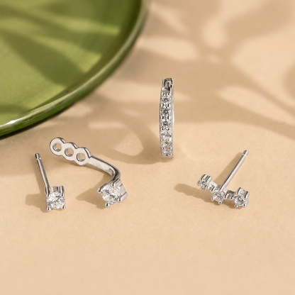 Set of silver earrings on a beige surface with a green plate in the background