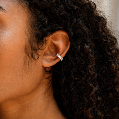 Close-up of an ear wearing a silver earring with curly hair.