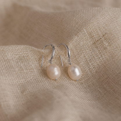 Pearl earrings on a beige fabric background