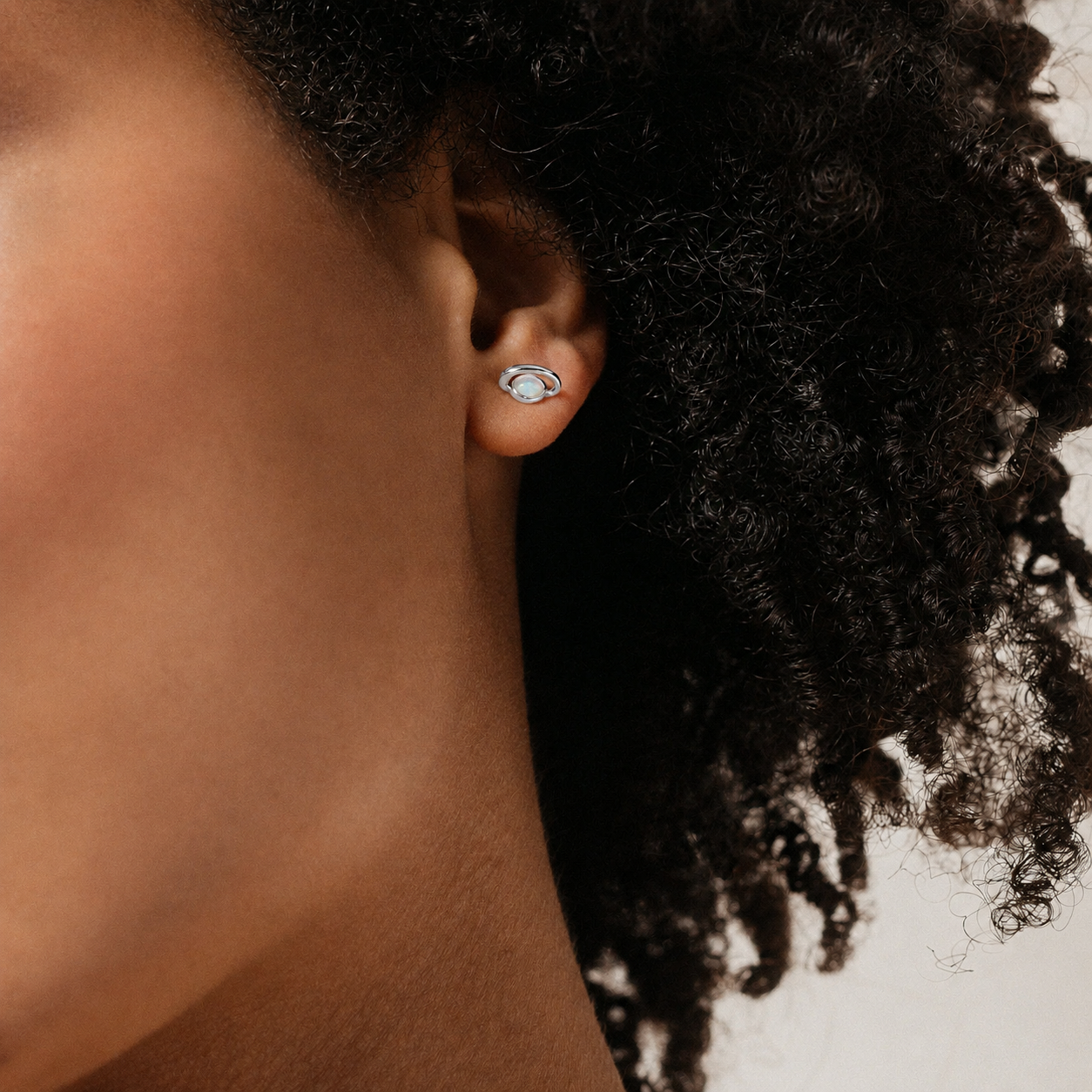 Close-up of an ear with a silver earring against a neutral background