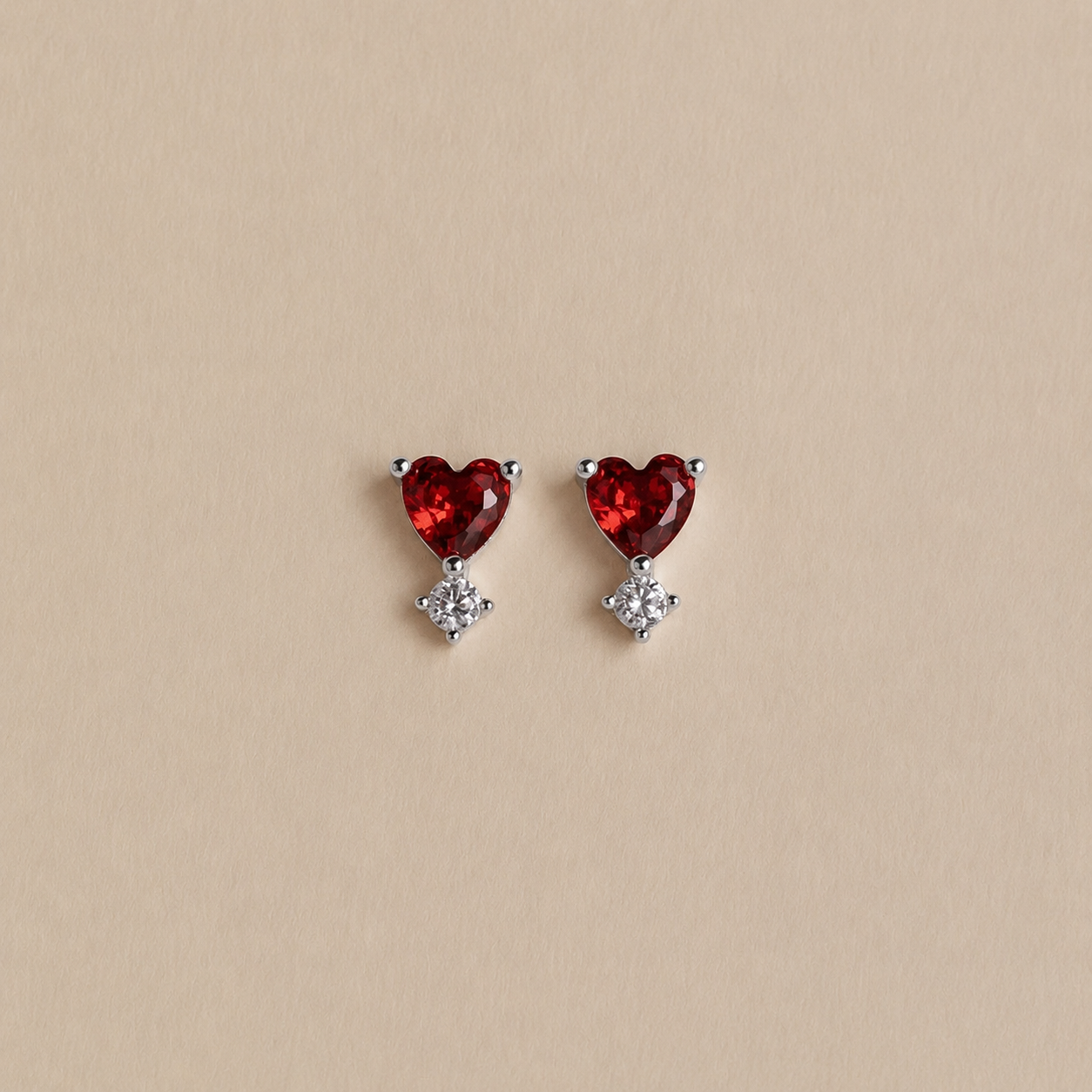Heart-shaped red gemstone earrings with small clear stones on a beige background
