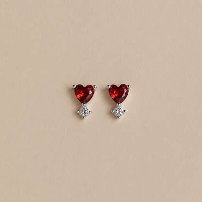 Heart-shaped red gemstone earrings with small clear stones on a beige background