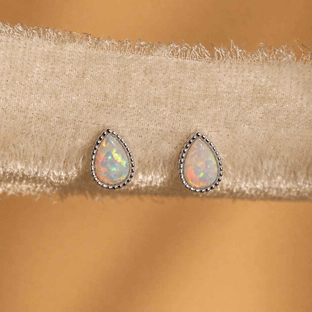 Teardrop-shaped opal earrings on a beige fabric background