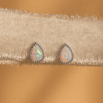 Teardrop-shaped opal earrings on a beige fabric background