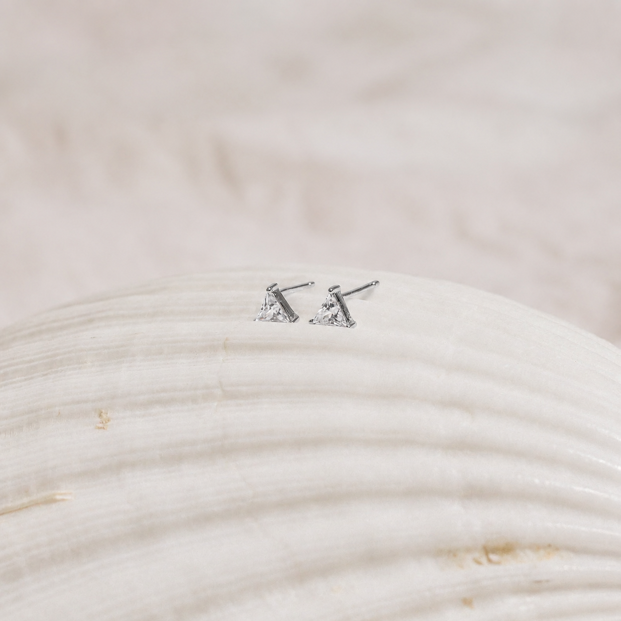 Pair of silver triangle stud earrings on a textured beige surface