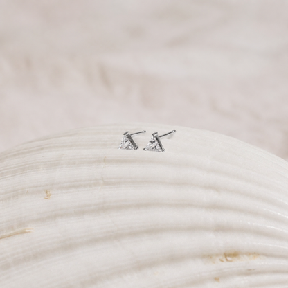 Pair of silver triangle stud earrings on a textured beige surface
