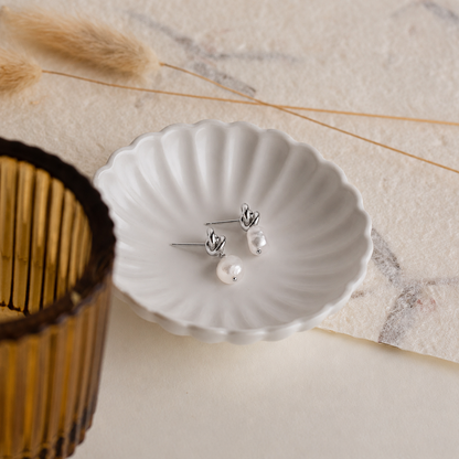 Pearl earrings on a white shell dish with dried grasses and a woven basket in the background.