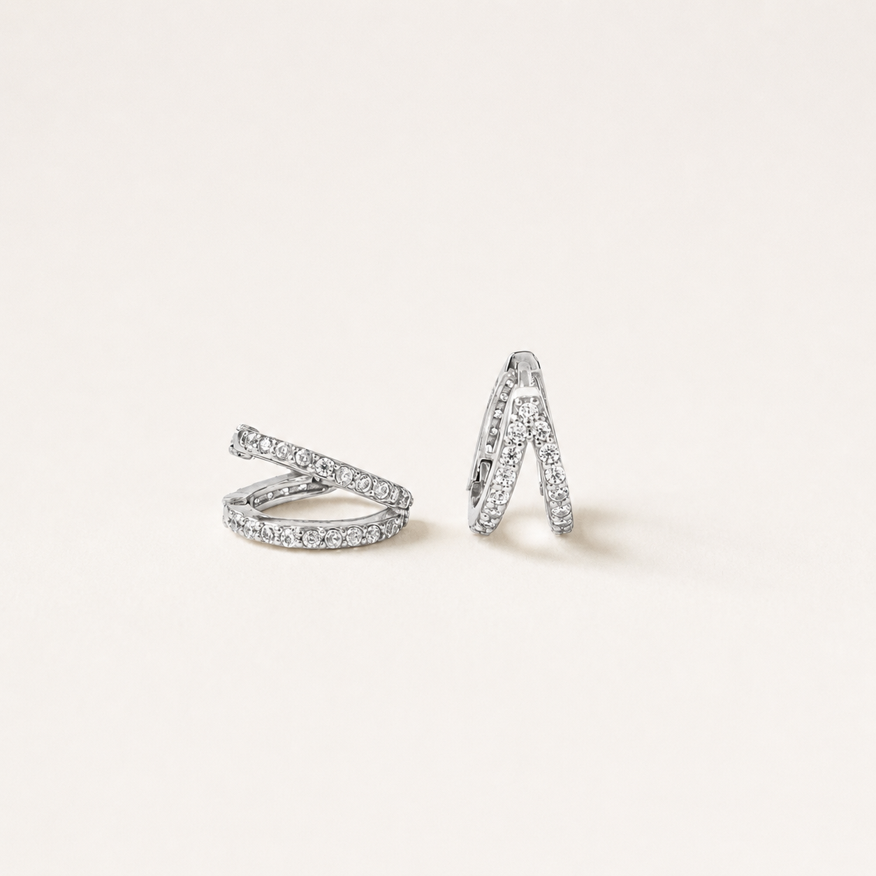 A pair of silver-toned wrap-style hoop earrings paved with small clear stones, displayed on a clean off-white background.