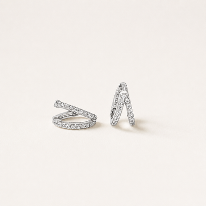 A pair of silver-toned wrap-style hoop earrings paved with small clear stones, displayed on a clean off-white background.