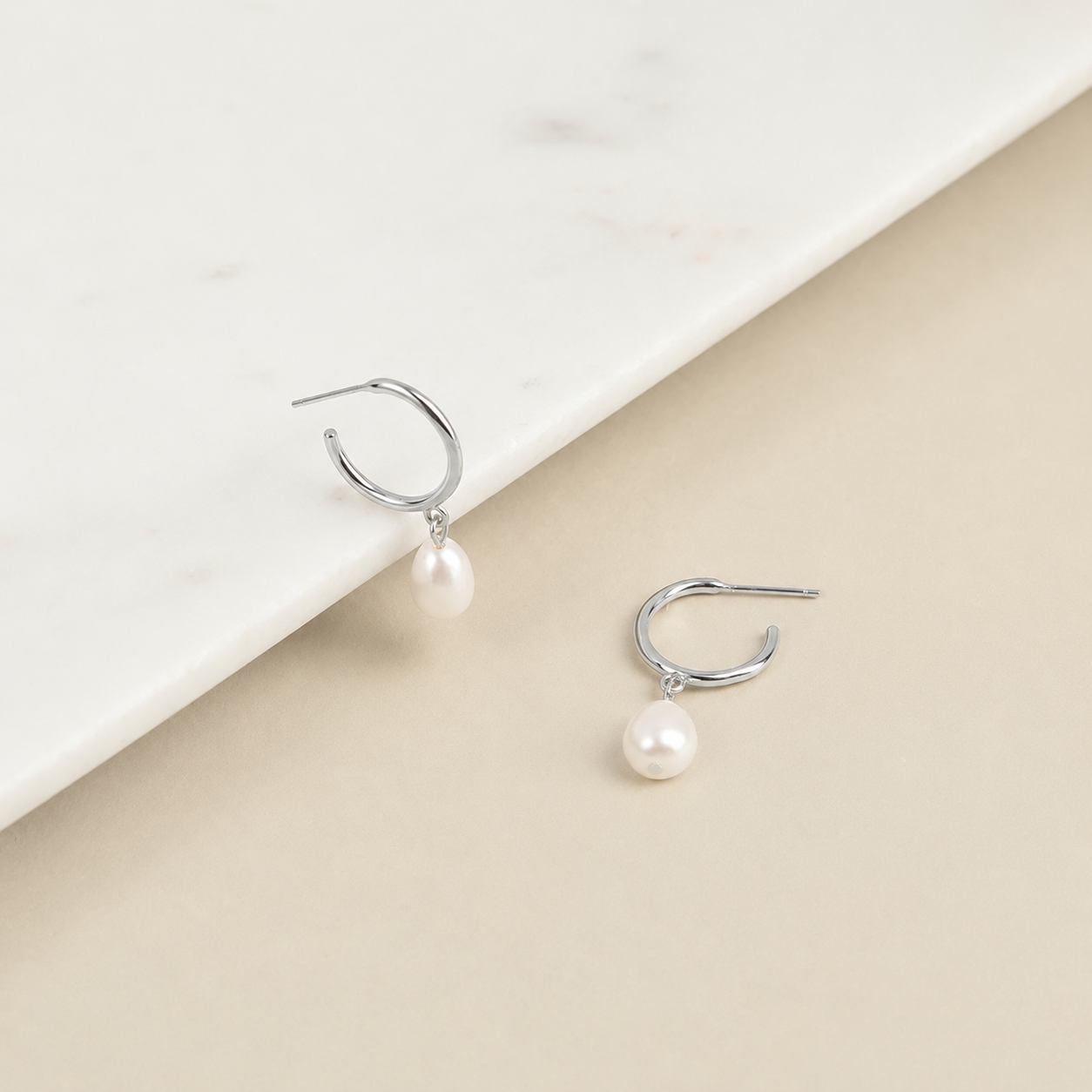 Pearl earrings on a beige and white background