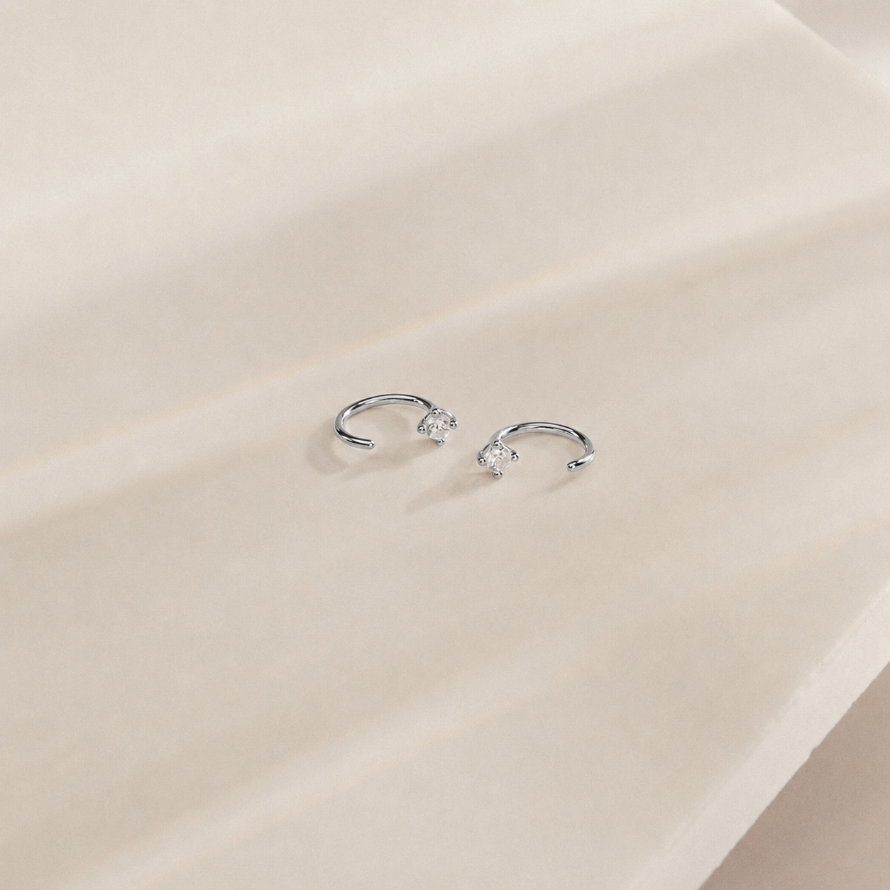 Silver earrings with small gemstones on a beige surface