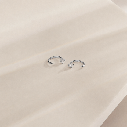 Silver earrings with small gemstones on a beige surface
