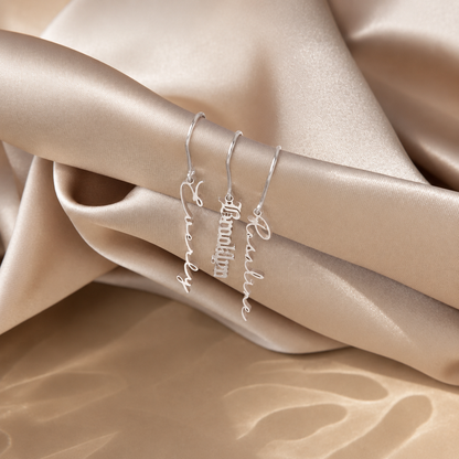 Three silver name bracelets on a beige fabric background