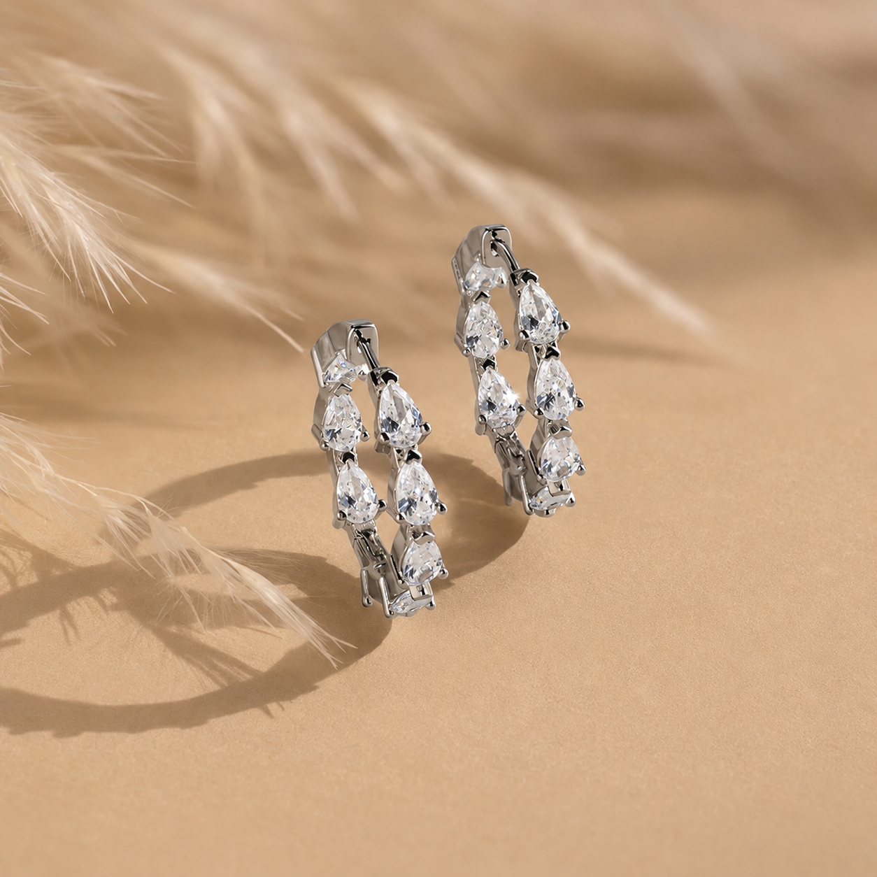 Pair of silver hoop earrings with clear gemstones on a beige sand background