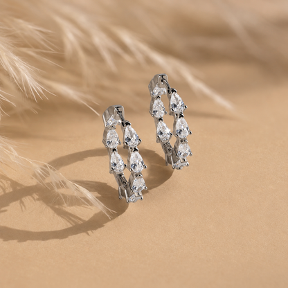 Pair of silver hoop earrings with clear gemstones on a beige sand background