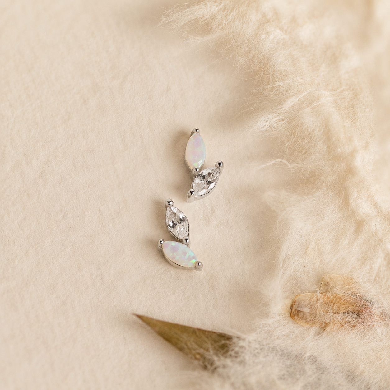 Pair of silver earrings with opal stones on a textured beige surface