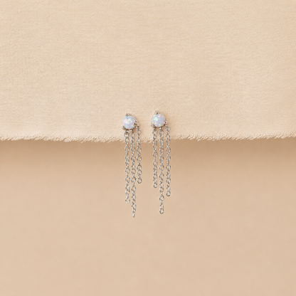 Pair of earrings with pearl-like stones and chain drops on a beige surface