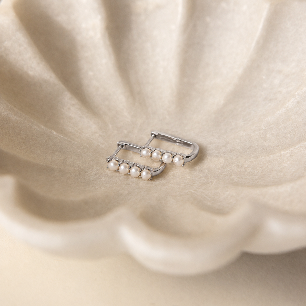 Silver earring with pearls on a beige fabric background