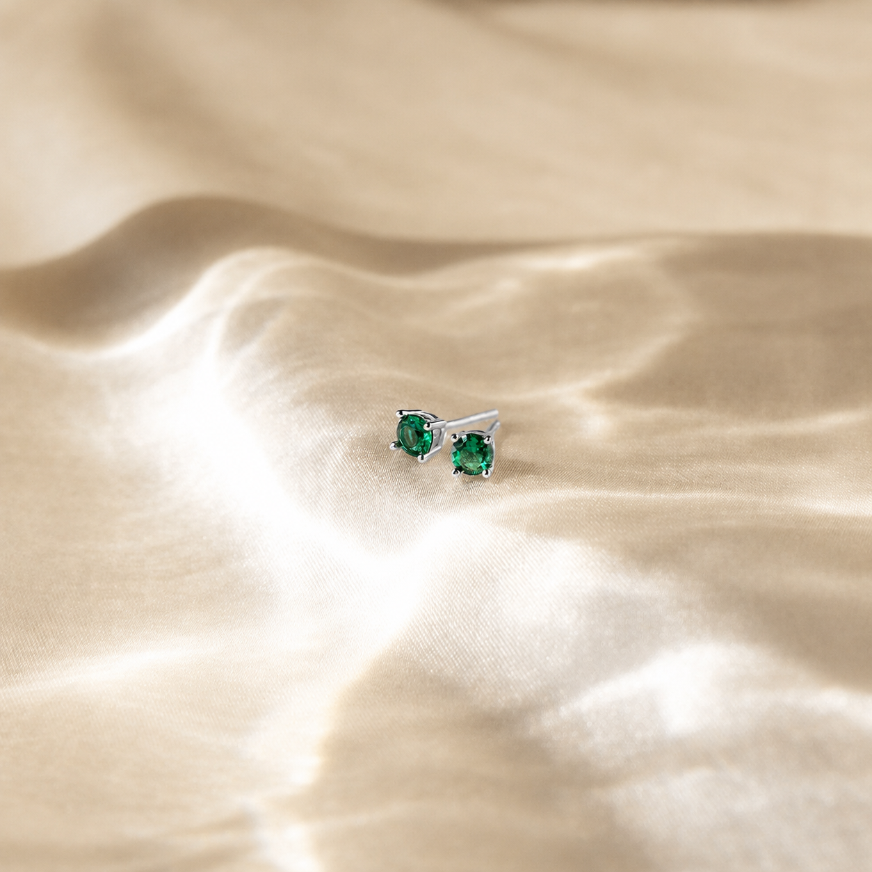 Silver earrings with green gemstones on a beige fabric background