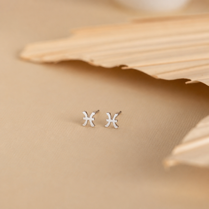 Silver zodiac earrings on a beige fabric background