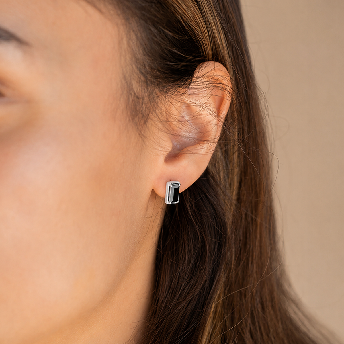 Close-up of an ear wearing a black and silver earring with a blurred background