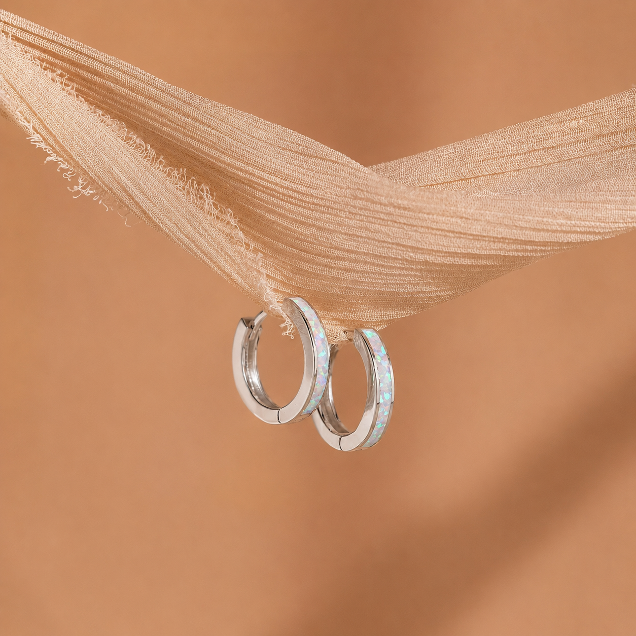 Silver hoop earrings with opal stones on a beige fabric background