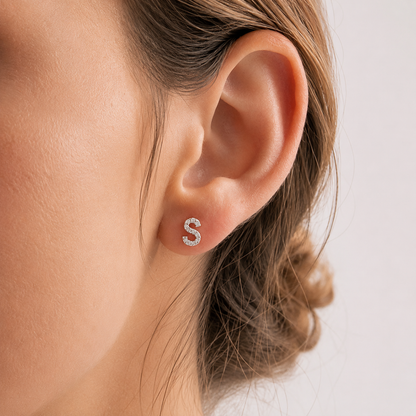 Close-up of an ear wearing a silver 'S' earring with a blurred background