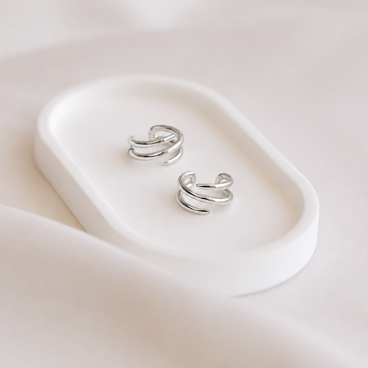 Pair of silver ear cuffs on a white dish with a soft pink background