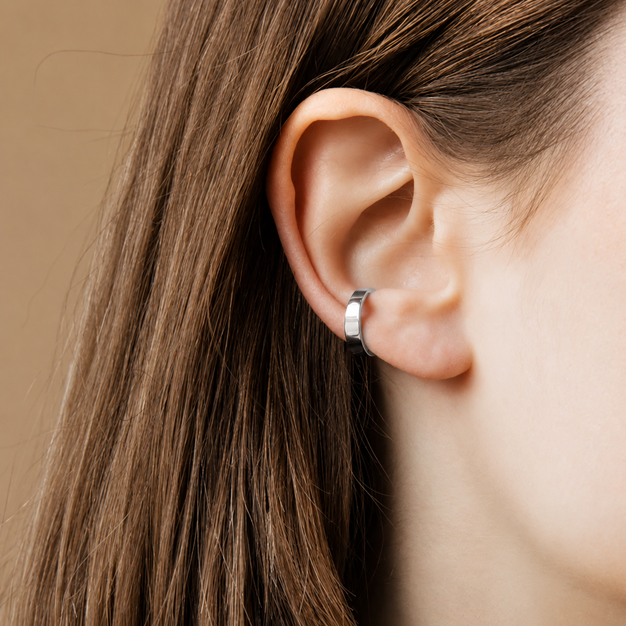 Close-up of an ear wearing a silver hoop earring with brown hair.