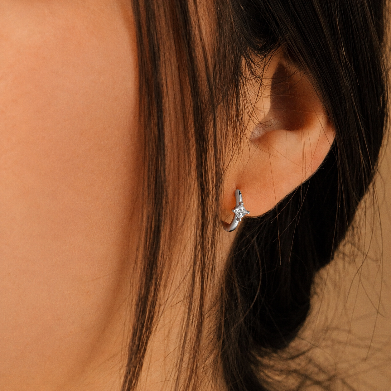 Close-up of an ear wearing a diamond earring with a blurred background