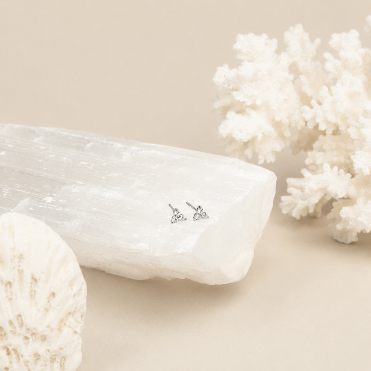 Pair of diamond earrings on a white stone with coral in the background