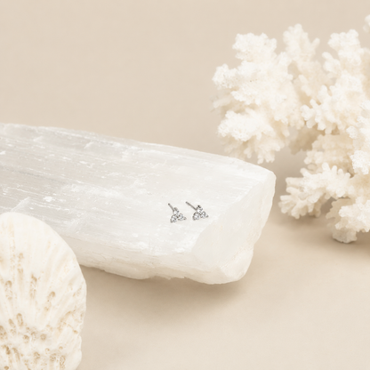 Pair of diamond earrings on a white stone with coral in the background