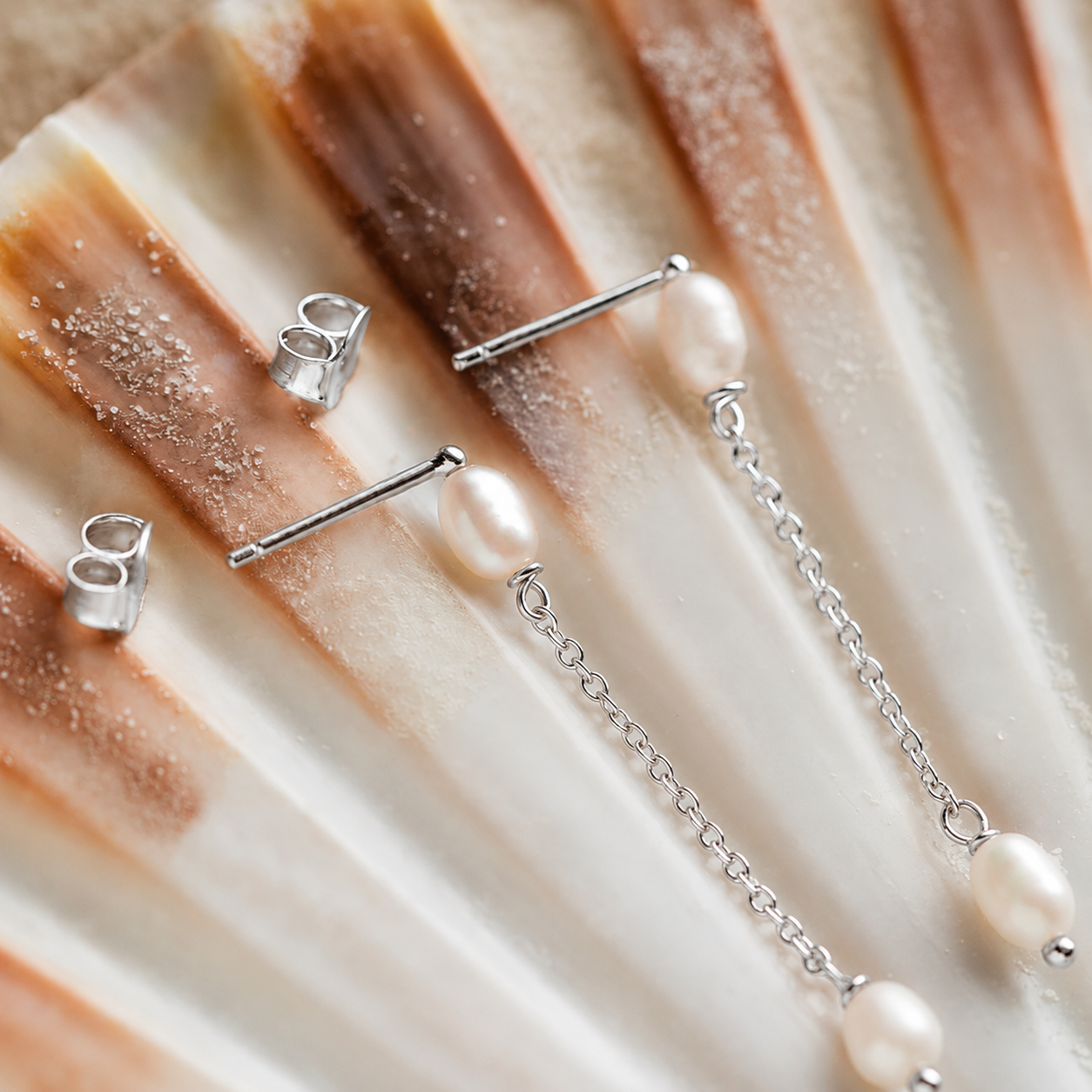 Silver jewelry set with earrings and a necklace on a textured beige surface