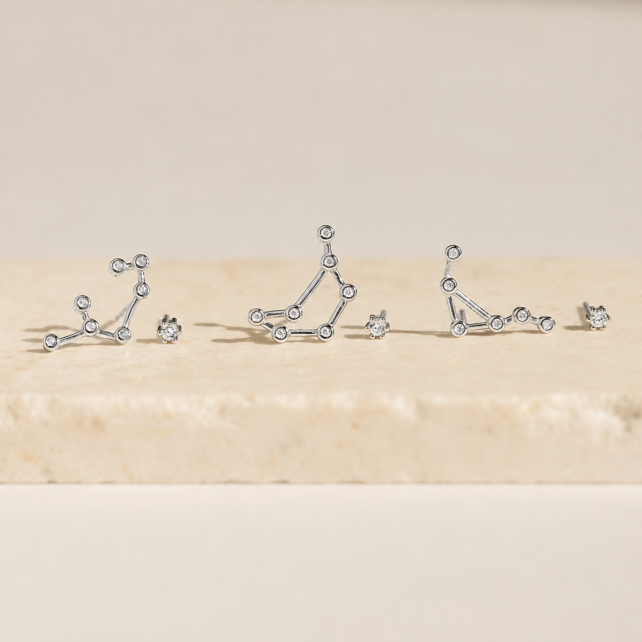 Silver constellation earrings on a beige surface