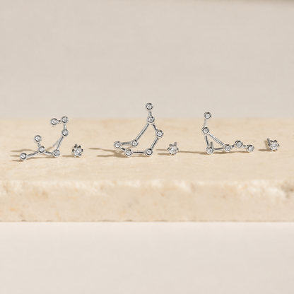 Silver constellation earrings on a beige surface