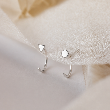 Silver earrings with geometric designs on a soft fabric background